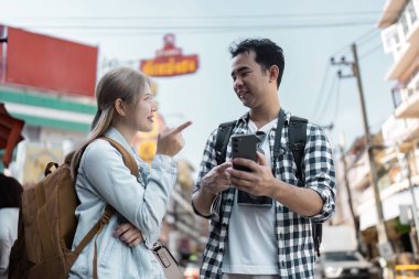 İki gezgin canlı bir şekilde sohbet ederken canlı bir şehir caddesini keşfediyor deneyimlerini paylaşıyor ve yolculuklarını planlıyorlar..