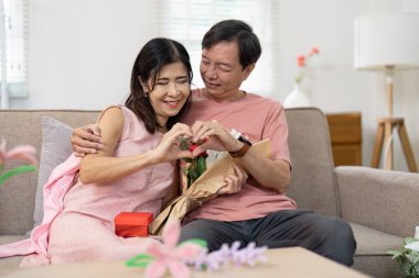 Elderly couple enjoying Valentines Day, exchanging gifts and flowers, sharing love and happiness in a warm home environment. clipart