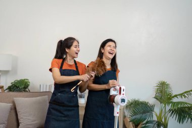 İki kadın oturma odasını modern aletlerle temizlemekten mutlu olurlar. Takım çalışması ve temiz, rahat bir ortam..