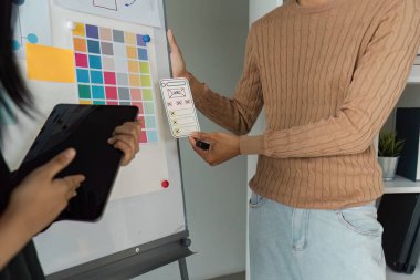 Kullanıcı arayüzü tasarımını tartışan yaratıcı profesyoneller, işbirlikçi bir çalışma alanında kablo çizimleri ve dijital araçları gösteriyorlar.