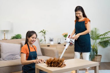 Ev işi yapan iki kadın, rahat bir oturma odasında modern temizlik aletleri kullanıyorlar..