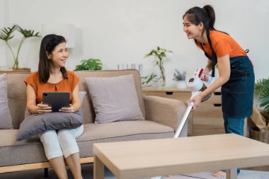 Havalı bir oturma odasında elektrikli süpürge kullanan hizmetçi tatmin olmuş bir müşteriyle iletişim kuruyor..