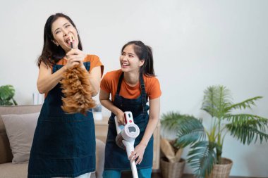 Two cheerful housekeepers cleaning a modern home, using a vacuum and duster, showcasing teamwork and efficiency in housework. clipart