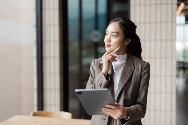 Modern ofis ortamında odaklanmış bir iş kadını, veri analizi ve stratejik planlama için bir tablet kullanıyor..