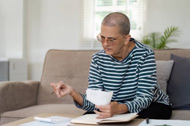 Finansal belgeleri inceleyen ve hesap makinesi kullanan yaşlı bir kadın güvenli ve rahat bir emeklilik planı yapıyor..