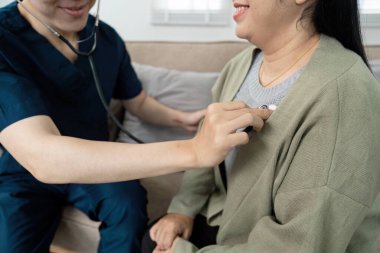 Önlüklü bir doktor ev ziyareti sırasında hastaların kalp atışlarını dinlemek için steteskop kullanır..