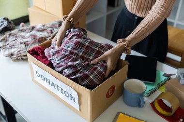 Woman arranging clothes in a donation box, symbolizing charity, community support, and giving back. clipart