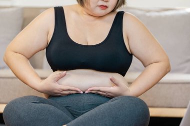 Ev ortamında rahat bir şekilde oturan, yoga ve beden farkındalığı ile uğraşırken özen ve farkındalık sergileyen iri yarı bir kadın..