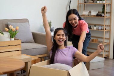 İki mutlu kadın, biri karton bir kutuda oturuyor ve diğeri onu itiyor, heyecan ve neşe dolu yeni evlerine taşınmalarını kutluyorlar..