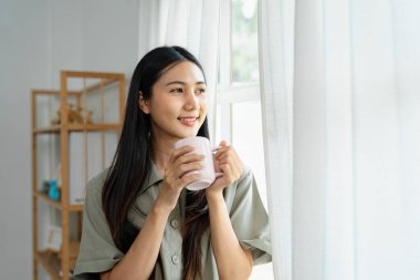Pencereden dışarı bakarken kahvesini yudumlayan mutlu bir kadın şık dekore edilmiş evinin içinde huzurlu bir anı kucaklıyor..