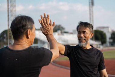 İki son sınıf öğrencisi güneşli bir günde açık hava egzersizi sırasında sağlık ve zindeliği beşlikle kutluyor..