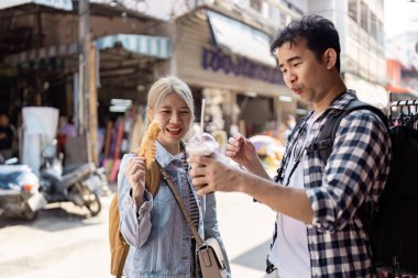 Neşeli bir çift, paylaşılan deneyimlerin neşesini somutlaştıran canlı bir sokak pazarını keşfederken lezzetli atıştırmalıklara ve ferahlatıcı içeceklere dalar..