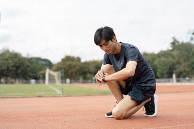 Kendini adamış genç bir adam koşu parkurunda mola verirken spor takip cihazını kontrol eder. İyileşme ve kendini geliştirme rutinini gösterir..