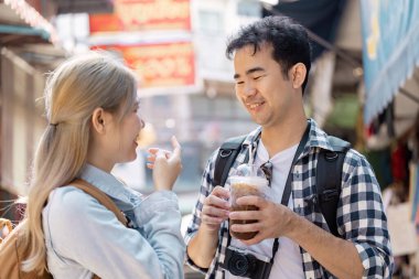 Neşeli bir çift, hareketli bir pazarda kahvelerini yudumlarken, arkadaşlığın ve açık havada eğlencenin özünü yakalar..