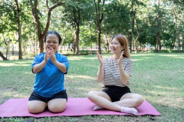 Açık hava egzersizlerini tamamladıktan sonra alkışlayan ve gülümseyen iki kadın, destekleyici ve canlı bir ortamda zindelik ve sağlığın sevincini sergiliyorlar..