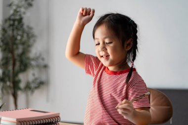 Öğrenme aktivitelerine katılan mutlu bir çocuk, elinde bir kalem ve yanında eğitimin keyfini simgeleyen bir defterle yaratıcılık ve neşe sergiliyor..
