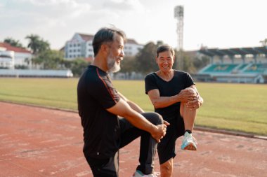 Pistte esneme egzersizleri yaparken gülümseyen iki son sınıf öğrencisi, refahı, dostluğu ve sonraki yıllarda aktif kalmanın keyfini vurguluyor..