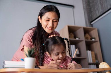 İlgili bir anne, öğrenim faaliyetleri sırasında çocuğuna destek olur. Eğitim bağını sembolize eden bir çizim üzerinde çalışırken yaratıcılığı ve bağlılığı teşvik eder..