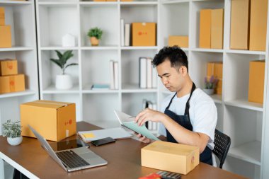 Odaklanmış bir girişimci, çevrimiçi satış ve küçük işletme işlemlerinin hızını sembolize eden paketler ve bir dizüstü bilgisayarla çevriliyken notları gözden geçirir.