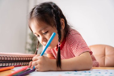 Kendini sanatına adamış bir çocuk, yaratıcılığını göstermek için renkli işaretler kullanıyor, not defterleri ve çizim materyalleriyle çevrili, öğrenme sevincini vurguluyor..