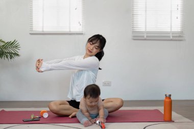 Bir anne, bebeği yanında sakin ve besleyici bir çevreyle oynarken yoga minderinin üzerinde esneme egzersizlerinden zevk alır..