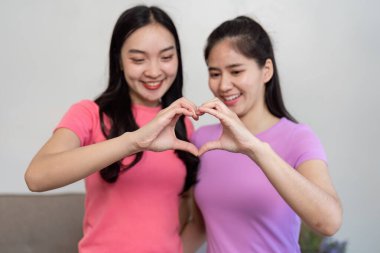 İki kadın elleriyle bir kalp şekli yaratıyor. Hareket halindeyken sevgilerini ve bağlantılarını gösteriyorlar. Birlik ve neşeyi sembolize ediyorlar..