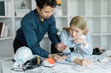 İki profesyonel akıllı telefondan proje planlarını tartışırken plan ve tasarımları gözden geçirir, ekip çalışması ve inşaat yönetimindeki etkili iletişimi gözler önüne serer.