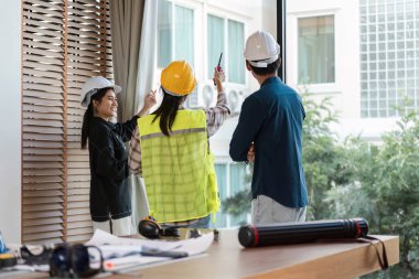 Sert şapka ve güvenlik yelekleri giyen bir grup inşaat işçisi, proje detaylarını parlak ve modern bir çalışma alanında tartışıyor, takım çalışması ve planlama sergiliyor.