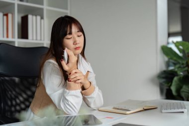 Genç bir bayan iş kadını ofisinde masasında otururken stresli görünüyor, iş sorumluluklarını ve teslim tarihlerini yansıtıyor..