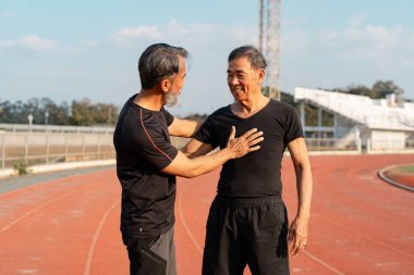 İki kıdemli adam pistte destekleyici bir anı paylaşıyor, arkadaşlığın önemini ve sağlıklı bir yaşam tarzını sürdürmedeki cesaretlendirmeyi vurguluyorlar..