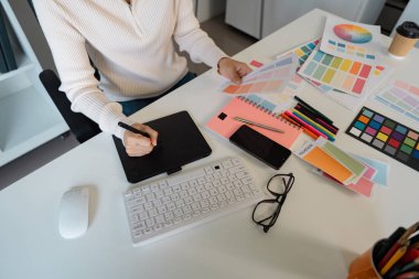 Masasında, renk paletleri, çizimler ve dijital araçlarla çevrili yaratıcı projeler üzerinde çalışan odaklanmış bir grafik tasarımcısı tasarım sürecini sergiliyor..