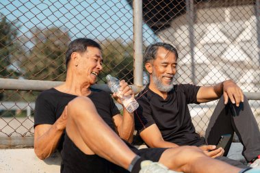 İki yaşlı adam neşeli bir anı paylaşıyor. Parkta güneşli bir günde birlikte su içip dinleniyorlar. Sağlıklı ve aktif bir yaşam tarzını destekliyorlar..