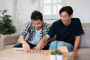 Bir LGBTQ çifti sıcak ve davetkar bir oturma odasıyla çevrili kahve masasında bozuk para organize ederken neşeli bir anı paylaşıyor..