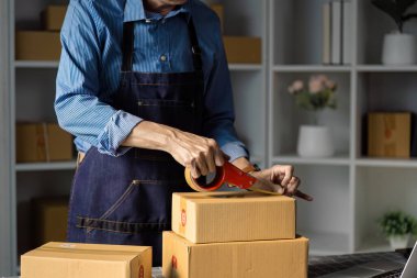 Çağdaş bir çalışma alanında kaset kullanarak, çevrimiçi satış ve sevkiyatlara hazırlanan bir e-ticaret işçisi kasetleri güvenli bir şekilde paketliyor..