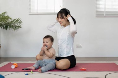 Evde bebeğiyle birlikte yoga yapan bir anne, evde rahat bir ortamda müzik dinlerken birlikte anın tadını çıkarıyor..