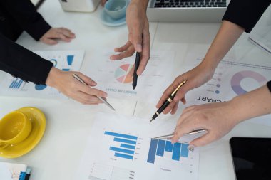 Ortak bir iş toplantısında finansal tablolar ve verileri inceleyen çeşitli profesyoneller, takım çalışması ve analizi vurguladılar.