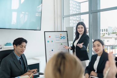 Çeşitli bir iş ekibi bir sunum yapıyor, finansal görüşleri paylaşıyor ve çağdaş bir ofis ortamında işbirliğini teşvik ediyor.