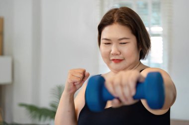 Kararlı bir Asyalı kadın evde güç egzersizi yapıyor, kendini sağIık yolculuğuna adamış ve güçlendirmiş..