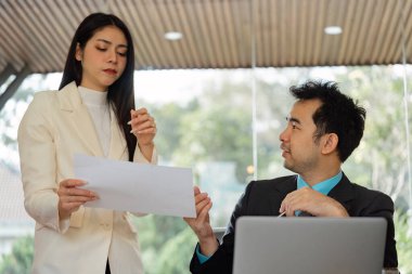 İki iş adamı, şirket ortamında işbirliği ve takım çalışmasının vurgulandığı çağdaş bir ofiste proje belgeleri hakkında ayrıntılı bir tartışmaya giriştiler..