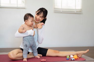 Asyalı bir anne yürümeye yeni başlamış çocuğuyla keyifli bir anı paylaşırken spor yapıyor, spor yapıyor, spor yapıyor ve günlük rutinlerini geliştiriyor..