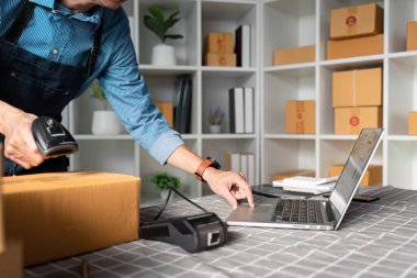 Bir e-ticaret girişimcisi barkod tarayıcısı ve dizüstü bilgisayarıyla aktif olarak envanteri yönetiyor ve çevrimiçi satışın dijital yönünü gösteriyor..