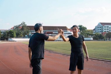 Pistteki çalışmalarını tamamladıktan sonra yumruk tokuşturan iki yaşlı adam, aktif yaşlanma içindeki dostluk ve refahı vurguluyor..