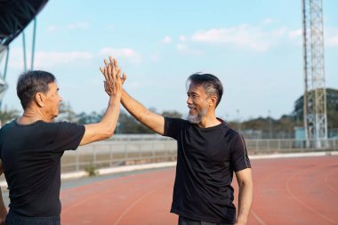 Pistte başarılı bir çalışmadan sonra beşlik çakan iki neşeli yaşlı adam, aktif yaşlanma içindeki dostluk ve refahı vurguluyor..
