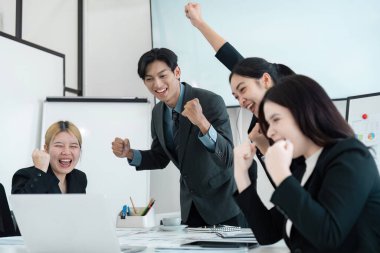 Heyecanlı bir iş ekibi başarılarını neşeli ifadelerle kutluyor ve şirket toplantısında yumruklarını kaldırıyor..