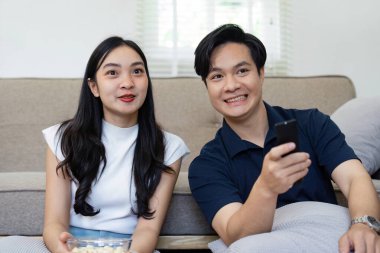 Film gecesi atıştırmalıkların tadını çıkarırken kameraya gülümseyen bir çift. Sıcak bir oturma odasında keyifli anlarını vurguluyorlar..