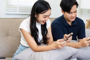 Bir çift telefonlarını kullanırken neşeli bir anı paylaşıyor, rahat bir ev ortamında bağlantılarını ve zevklerini vurguluyor..