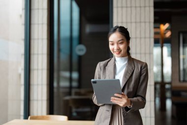 Neşeli profesyonel bir kadın ayakta ve tablet kullanıyor, ekranda gülümsüyor çağdaş dekor ve doğal ışıkla.