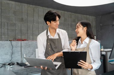 Bir barista ve kafe müdürü, modern bir kafe ortamında takım çalışmasını ön plana çıkaran bir dizüstü bilgisayar ve pano kullanarak yeni girişimler üzerinde büyük bir hevesle işbirliği içinde çalışmaktadır..