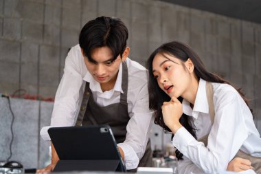 Odaklanmış bir barista ve kafe müdürü, modern kafelerinde bir tablet kullanarak performans analizi yapıyor, adanmışlık ve takım çalışması sergiliyor..