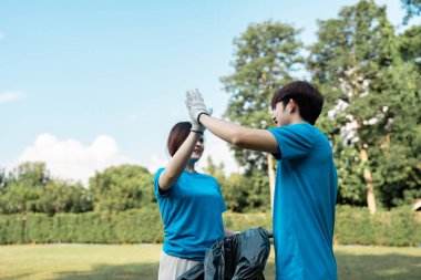 Mavi tişörtlü iki gönüllü arasında neşeli bir an. Çöpleri topladıktan sonra beşlik çakıyorlar. Toplumun ruhunu somutlaştırıyorlar..